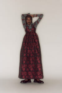 Girl wearing a gray striped sweater and a red floral maxi dress, standing with arms raised against a white background.