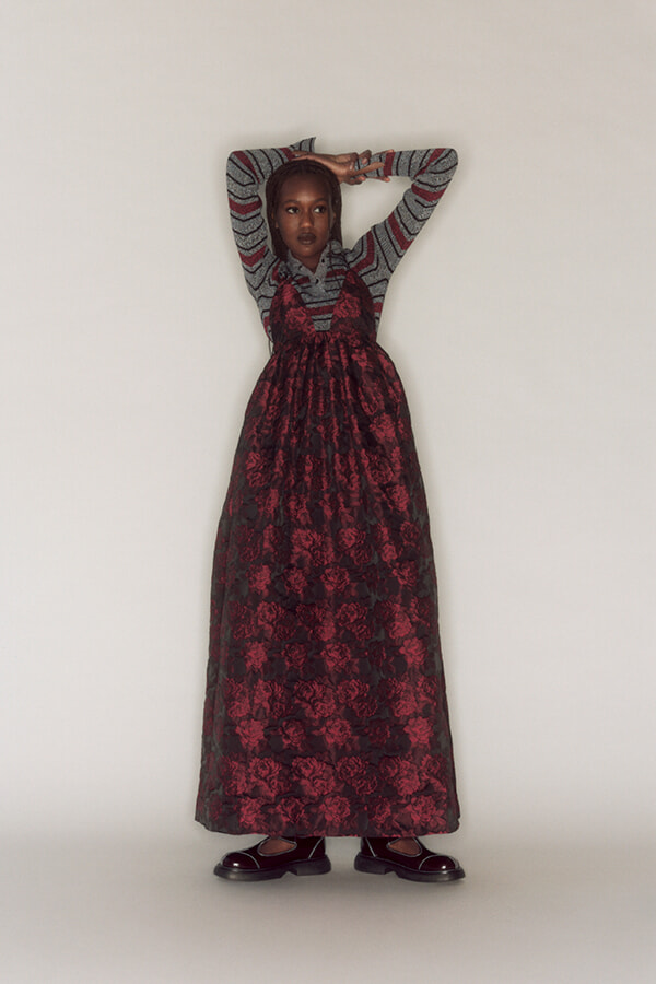 Girl wearing a gray striped sweater and a red floral maxi dress, standing with arms raised against a white background.