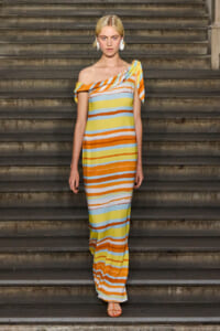 Woman wearing a colorful off-the-shoulder striped maxi dress standing on stone stairs, with sandals, looking forward.