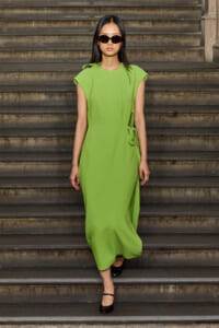 Model in a lime-green dress walking down stone steps, wearing black sunglasses and black heels.