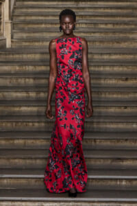 Full-body portrait of a Black woman in a red floral maxi dress standing on stone stairs, facing forward.