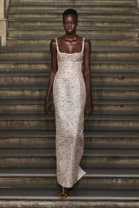 Model wearing a champagne-sequin, floor-length gown on stone stairs with yellow sandals visible at the bottom.
