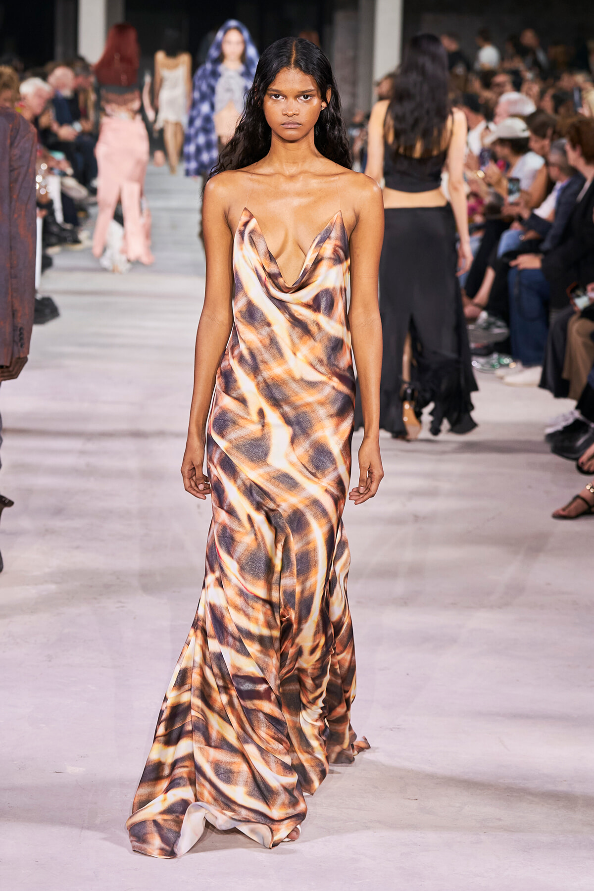 Model on a fashion-show runway wearing a draped, satin dress with an abstract brown-tan pattern.