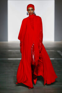 Model walks the runway in a full-length red ensemble with a matching head wrap and oversized silver earrings.