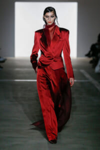 Female model on a runway wearing a bold red satin suit with an oversized blazer and wide-leg pants, looking forward