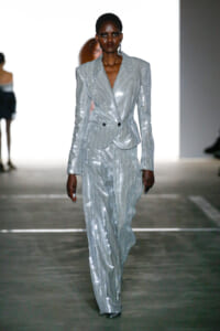 Model walking runway in a metallic silver pinstripe suit with a double-breasted blazer and wide-leg trousers, sequined finish catching the light