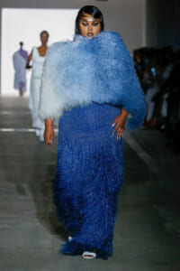 Model on a runway wearing a shimmering, beaded blue gown with a large pale-blue fluffy cape.