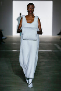 Model walks the runway in a white fluffy sleeveless dress, carrying a matching white plush clutch.