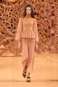 Runway model in peach-toned high-neck top with voluminous sleeves and matching wide-leg pants.