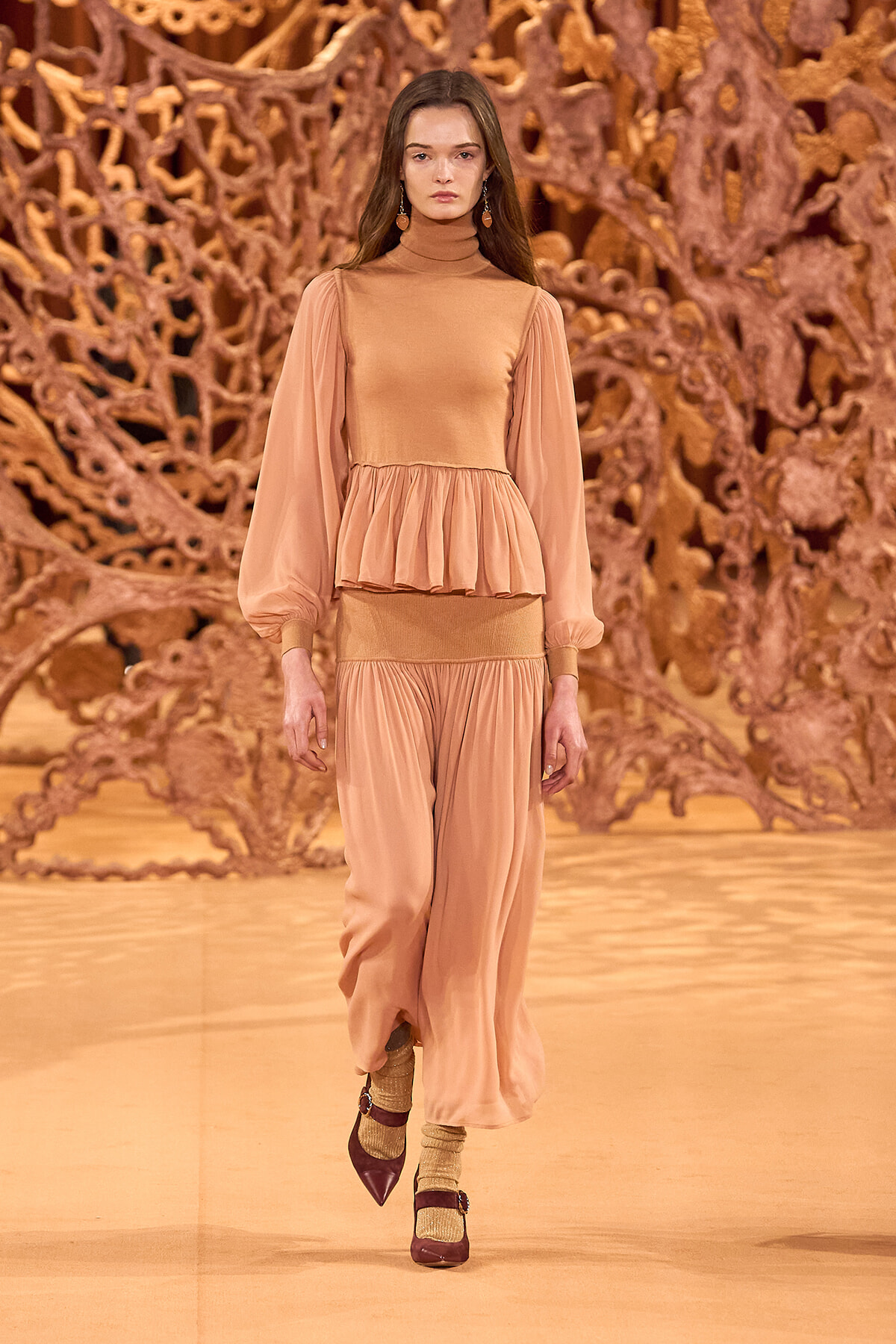 Runway model in peach-toned high-neck top with voluminous sleeves and matching wide-leg pants.