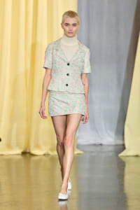 Model walks the runway in a mint green floral blazer and matching mini skirt with a cream turtleneck