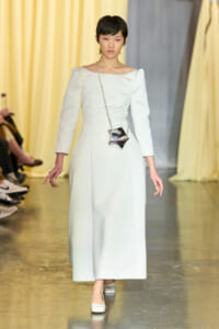 Model walks the runway wearing a pale blue long dress with a square neckline and puff sleeves, carrying a star-shaped metallic bag on a chain.