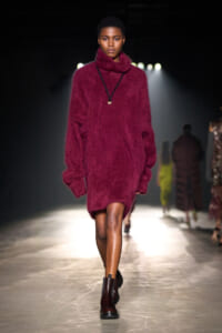 Model walks the runway in an oversized burgundy fuzzy knit turtleneck sweater with a pendant necklace.
