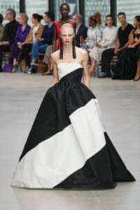 Model walks the runway in a strapless black‑and‑white color‑block ball gown with a voluminous skirt and bold makeup.