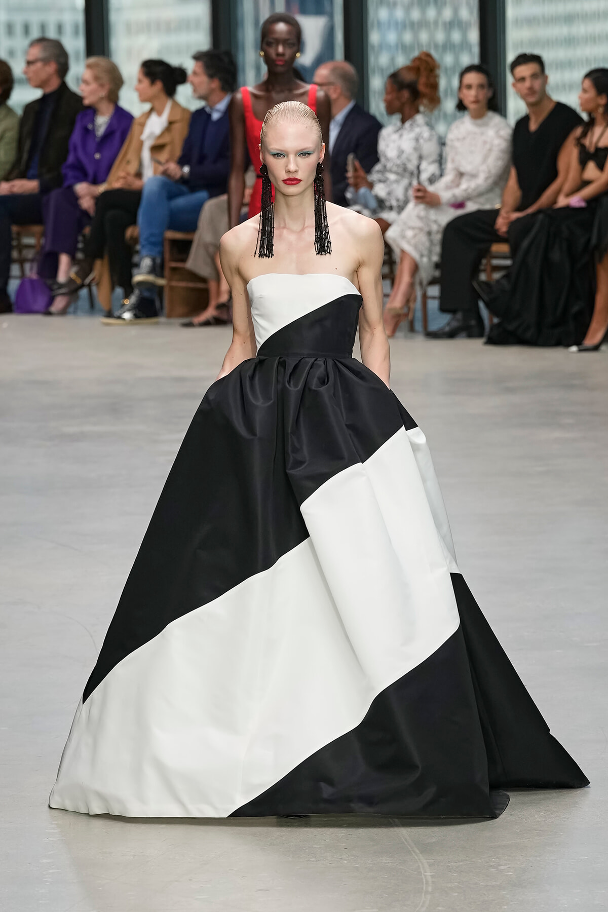 Model walks the runway in a strapless black‑and‑white color‑block ball gown with a voluminous skirt and bold makeup.