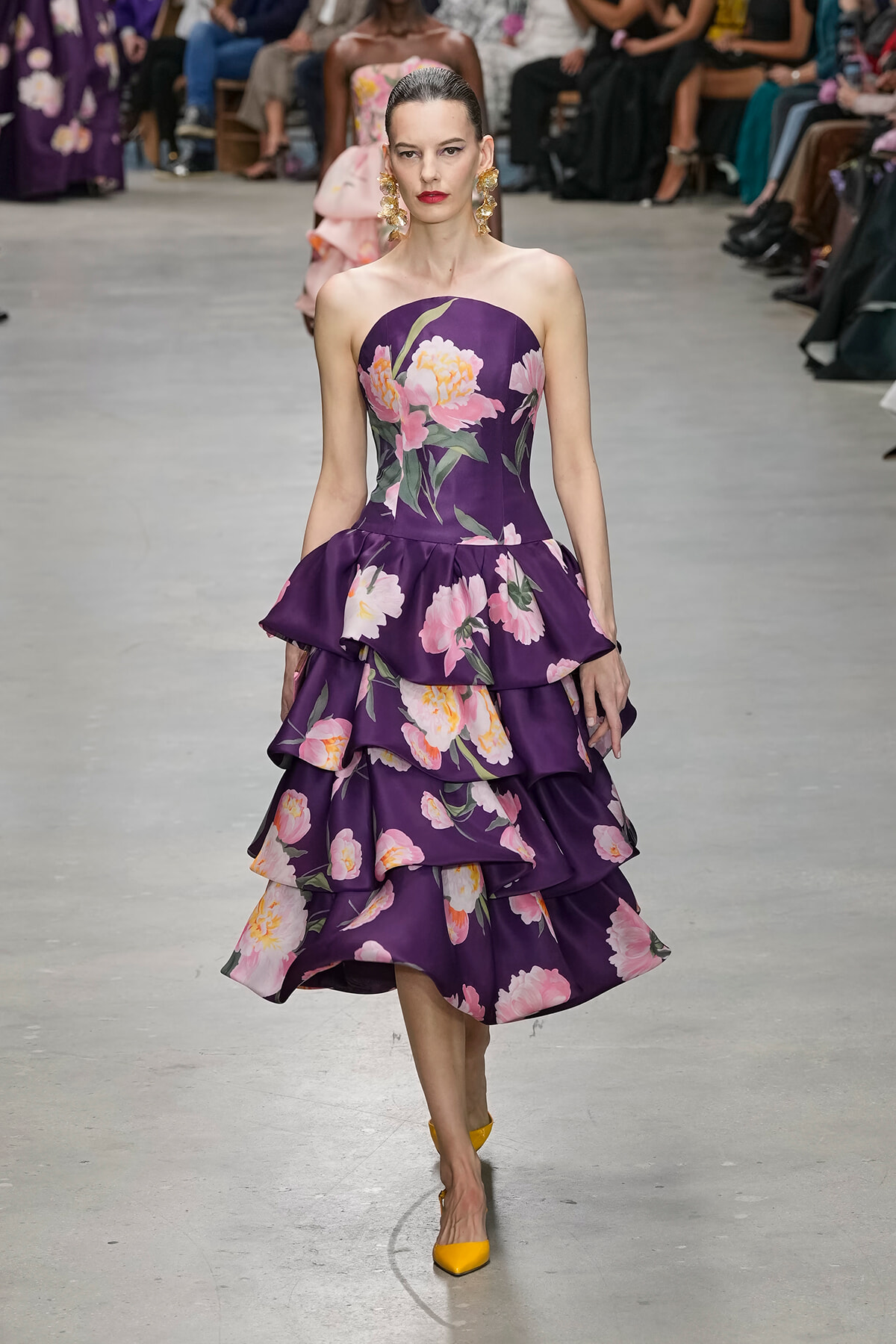 Model walks the runway in a purple strapless floral gown with tiered ruffles and yellow heels.