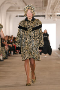 Model walks a fashion show wearing a leopard-print faux fur coat and matching hat.