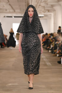 Model walking down a fashion runway in a gray leopard-print hooded cape over a matching dress, paired with black heels.