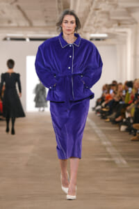 Model walks down runway in a cobalt velvet belted suit with white piping and white heels.