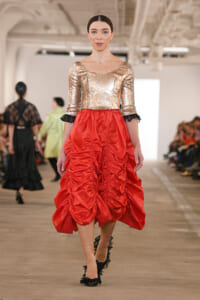 Model walking the runway in a gold sequin top paired with a voluminous red ruched skirt and black lace heels