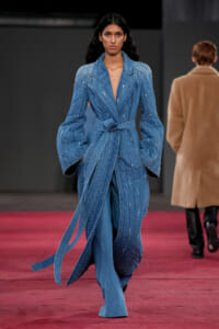 Female model walks the runway in a light-blue denim suit with a belt and oversized sleeves.