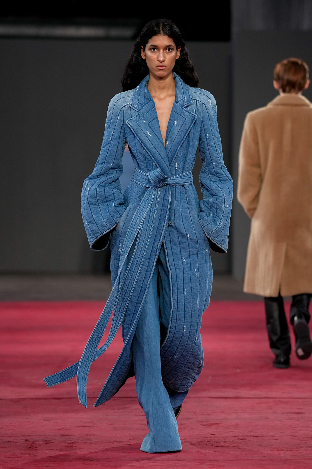 Female model walks the runway in a light-blue denim suit with a belt and oversized sleeves.