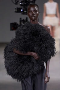 Model on a runway wearing a large black feathered shawl draped over the shoulders.