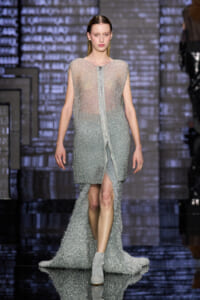 Model walks the runway in a sparkling silver beaded gown with a front zipper and long train.