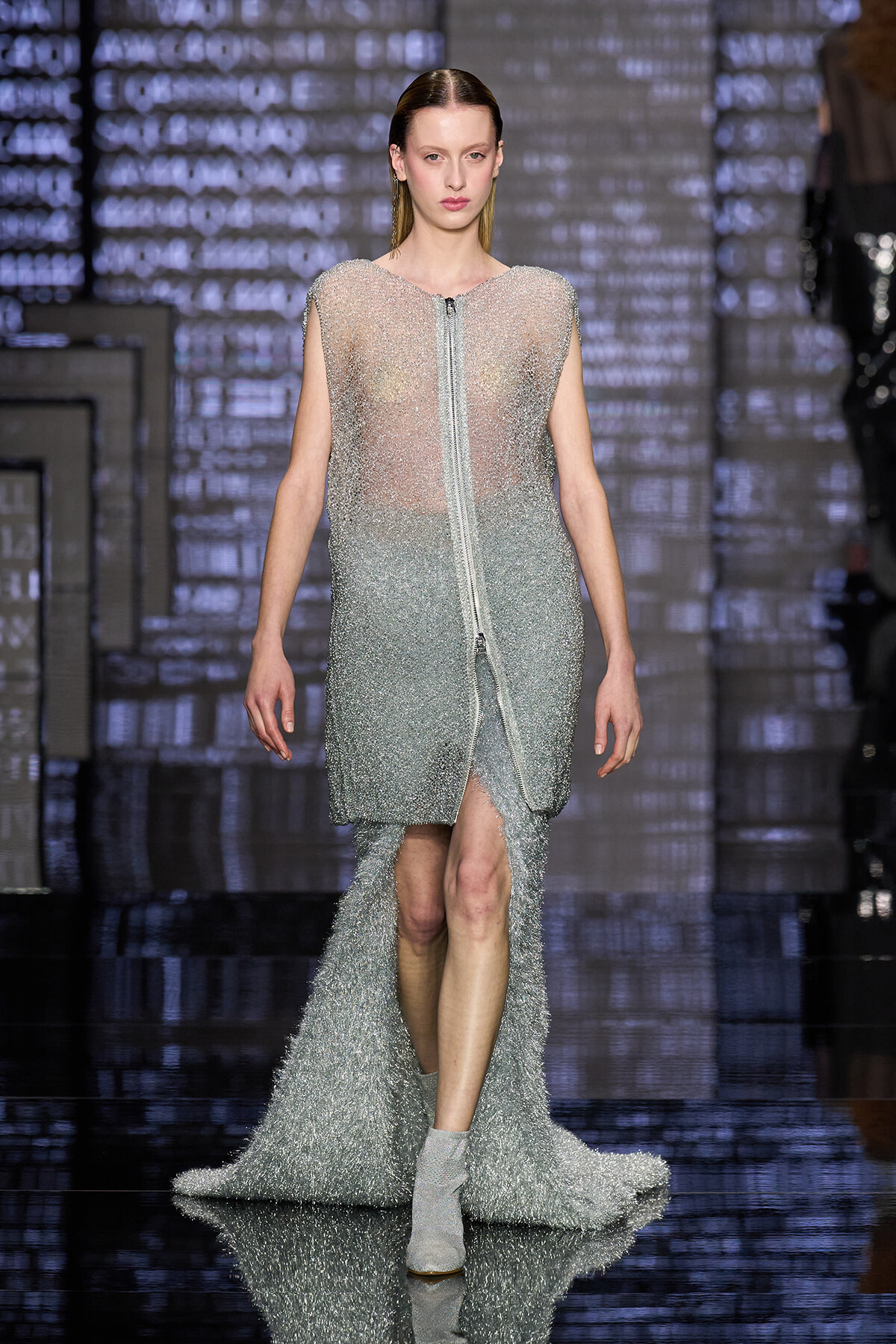 Model walks the runway in a sparkling silver beaded gown with a front zipper and long train.