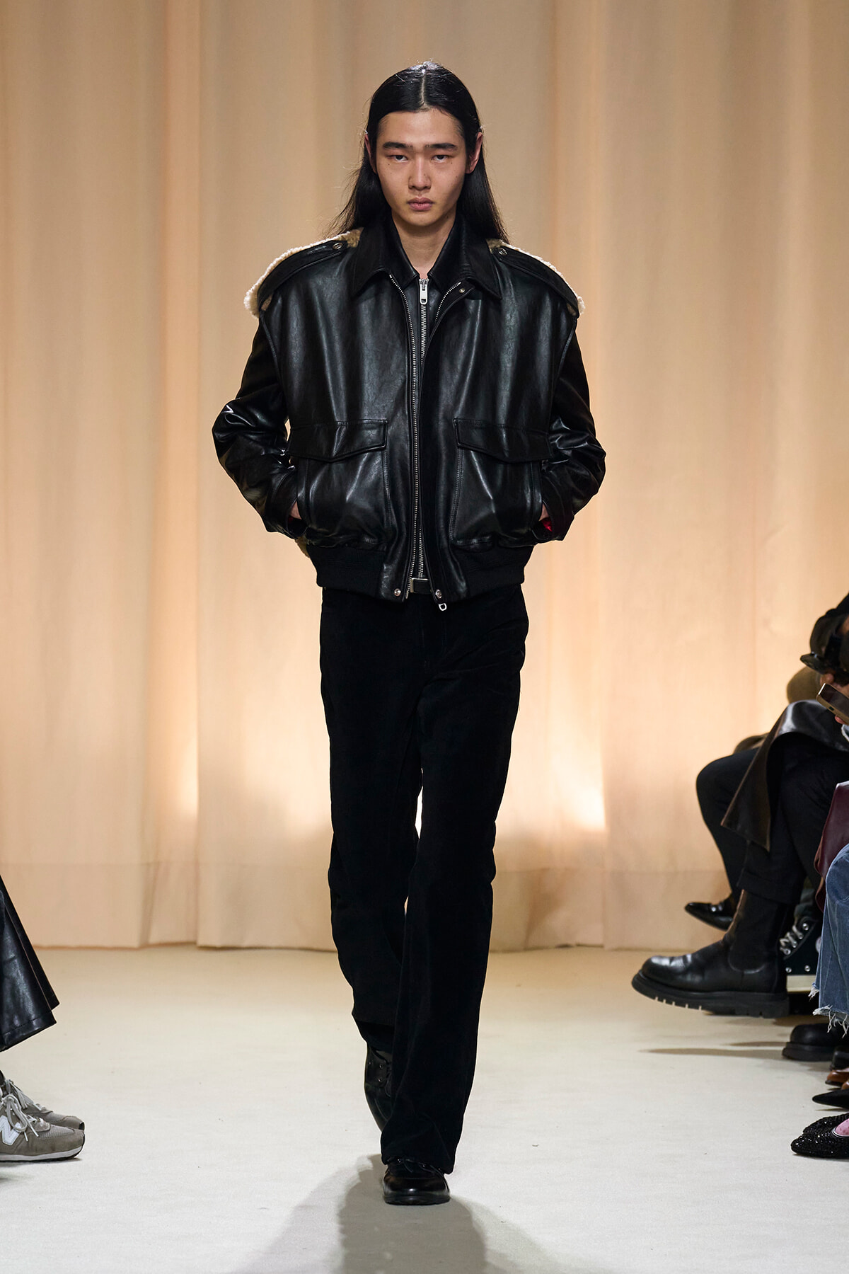Model walks the runway in a black leather bomber jacket with shearling accents and black pants.
