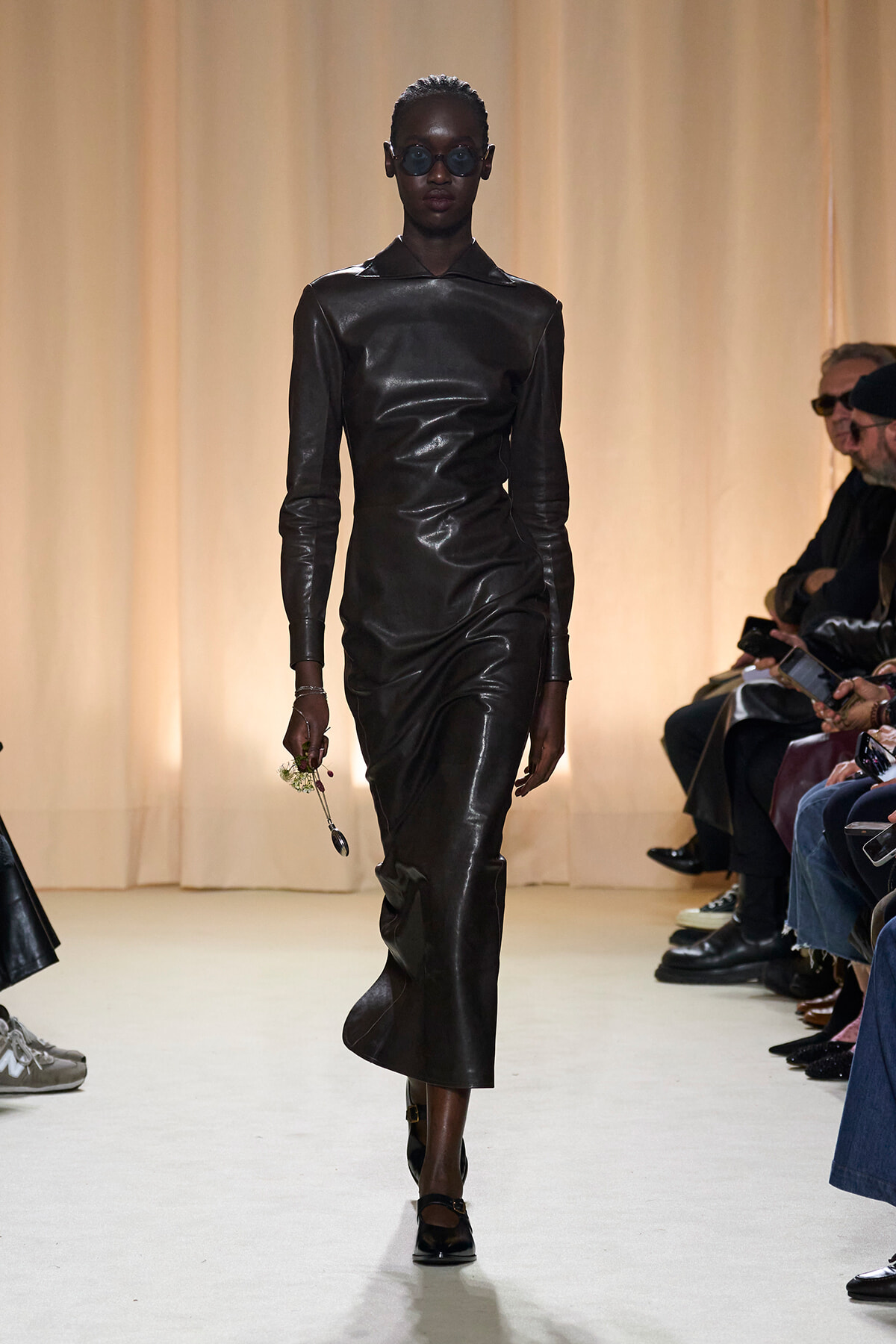 Model walking the runway in a black leather long-sleeve midi dress, wearing dark sunglasses.