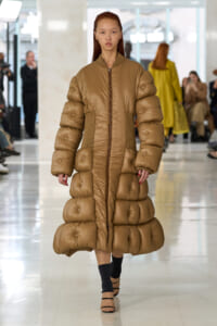 Model walks the runway in a long tan metallic quilted puffer coat with a central zipper