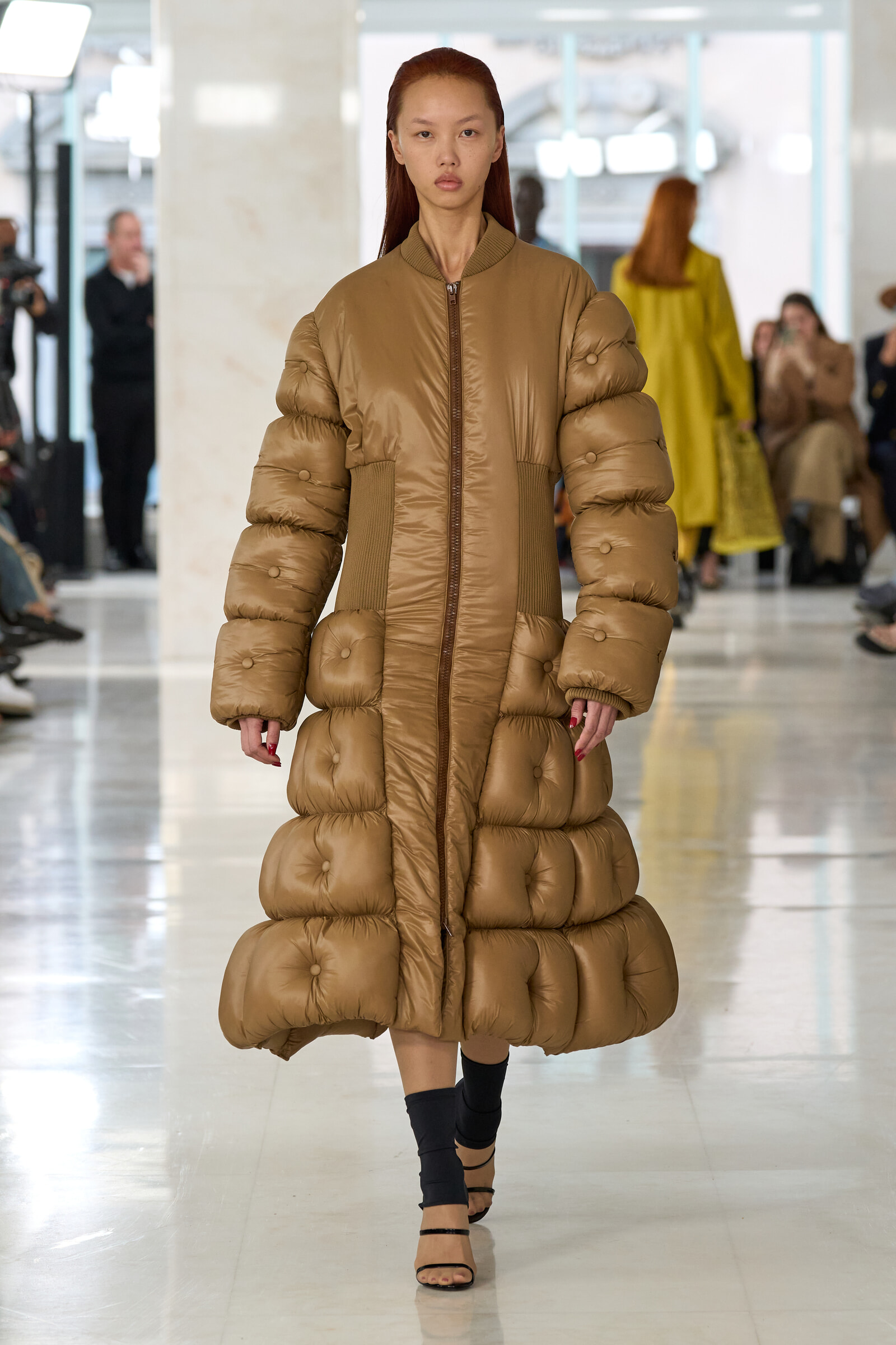 Model walks the runway in a long tan metallic quilted puffer coat with a central zipper