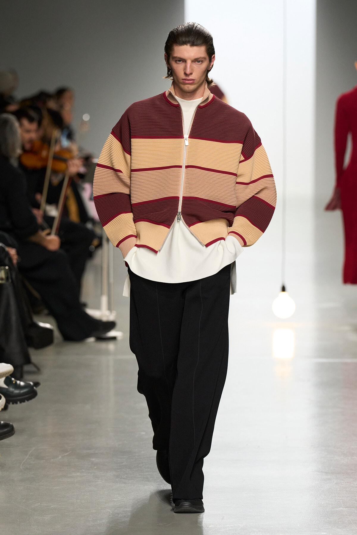 Male model wearing a burgundy, beige, and tan color-block zip cardigan over a white shirt on a fashion runway