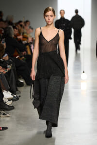 Model walking a fashion runway in a black sheer V-neck top with a glittery layered skirt set.