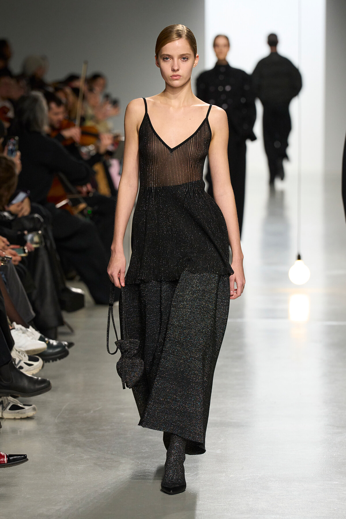 Model walking a fashion runway in a black sheer V-neck top with a glittery layered skirt set.