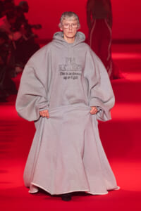 Person walking on a red runway wearing a large gray hoodie with the printed text: "I'M RETIRED (This is as dressed up as I get)"