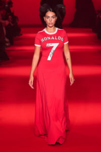 Model walks a red runway wearing a long red dress with a white-trim sports-jersey top that reads 'RONALDO' and the number 7.