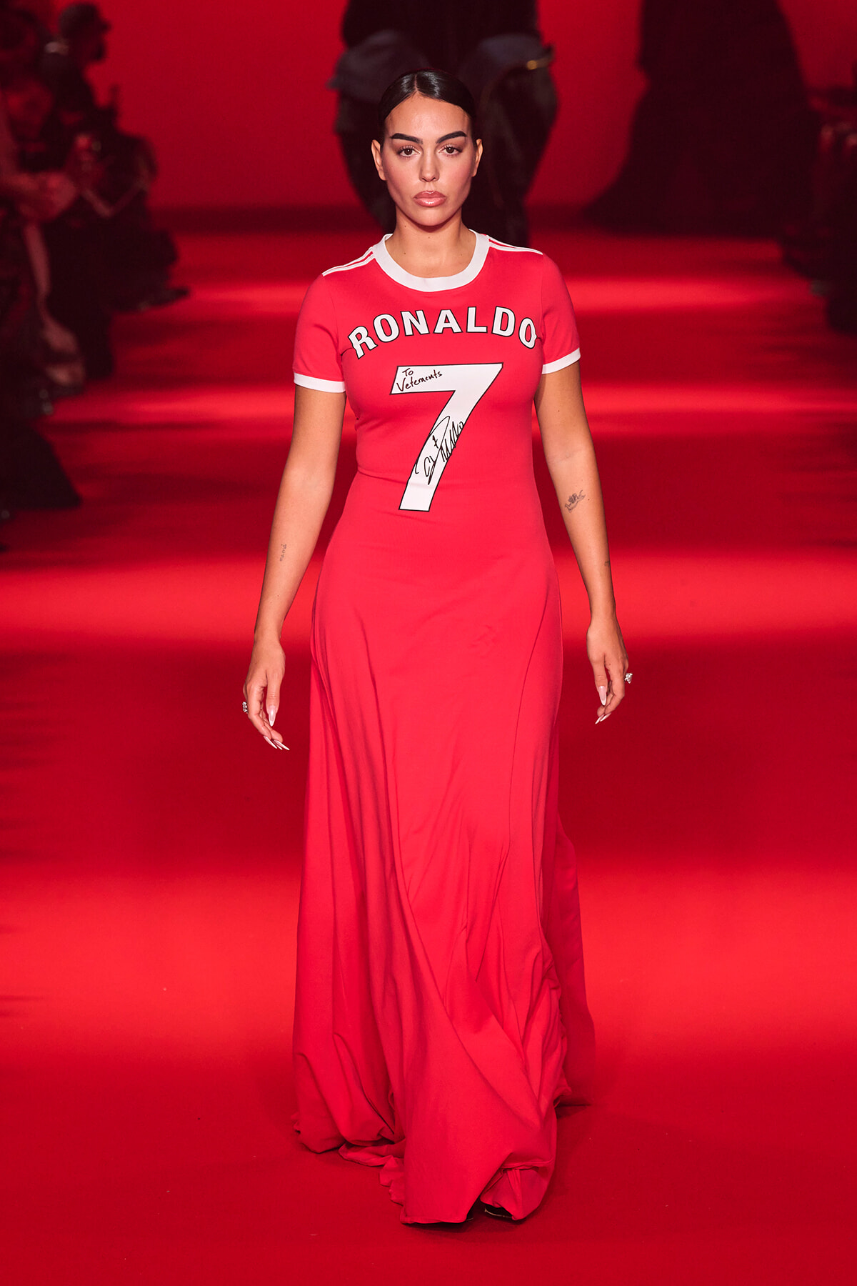 Model walks a red runway wearing a long red dress with a white-trim sports-jersey top that reads 'RONALDO' and the number 7.