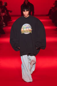 Model on a red-lit runway wearing an oversized black sweatshirt with a South Park graphic.