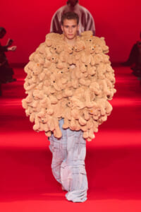 Model walks the red-runway wearing an oversized coat made of beige stuffed teddy bears.
