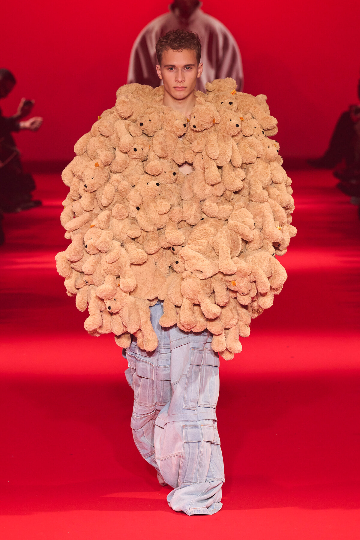 Model walks the red-runway wearing an oversized coat made of beige stuffed teddy bears.