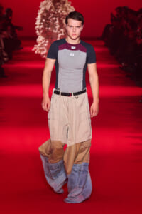 Male model walks a red runway wearing a color-block T-shirt and patchwork cargo pants.