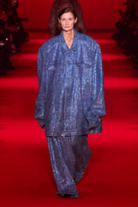 Model wearing a loose, blue sequin suit walking a red runway.