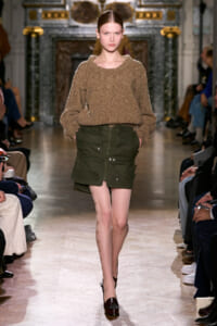 Model walks a runway wearing a chunky brown knit sweater and olive green cargo mini skirt.