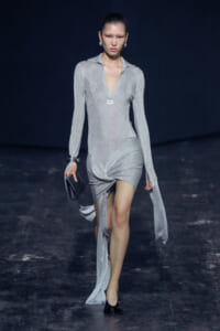 Model walks the runway in a silver glittery long-sleeve dress with a plunging V neckline and twisted front hem.