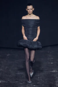 Model on a runway in a navy off-shoulder, ruched dress with a voluminous bubble hem and sparkly silver heels.