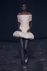 Runway model in a pale pink off-shoulder dress with a large puffed skirt walking the catwalk.