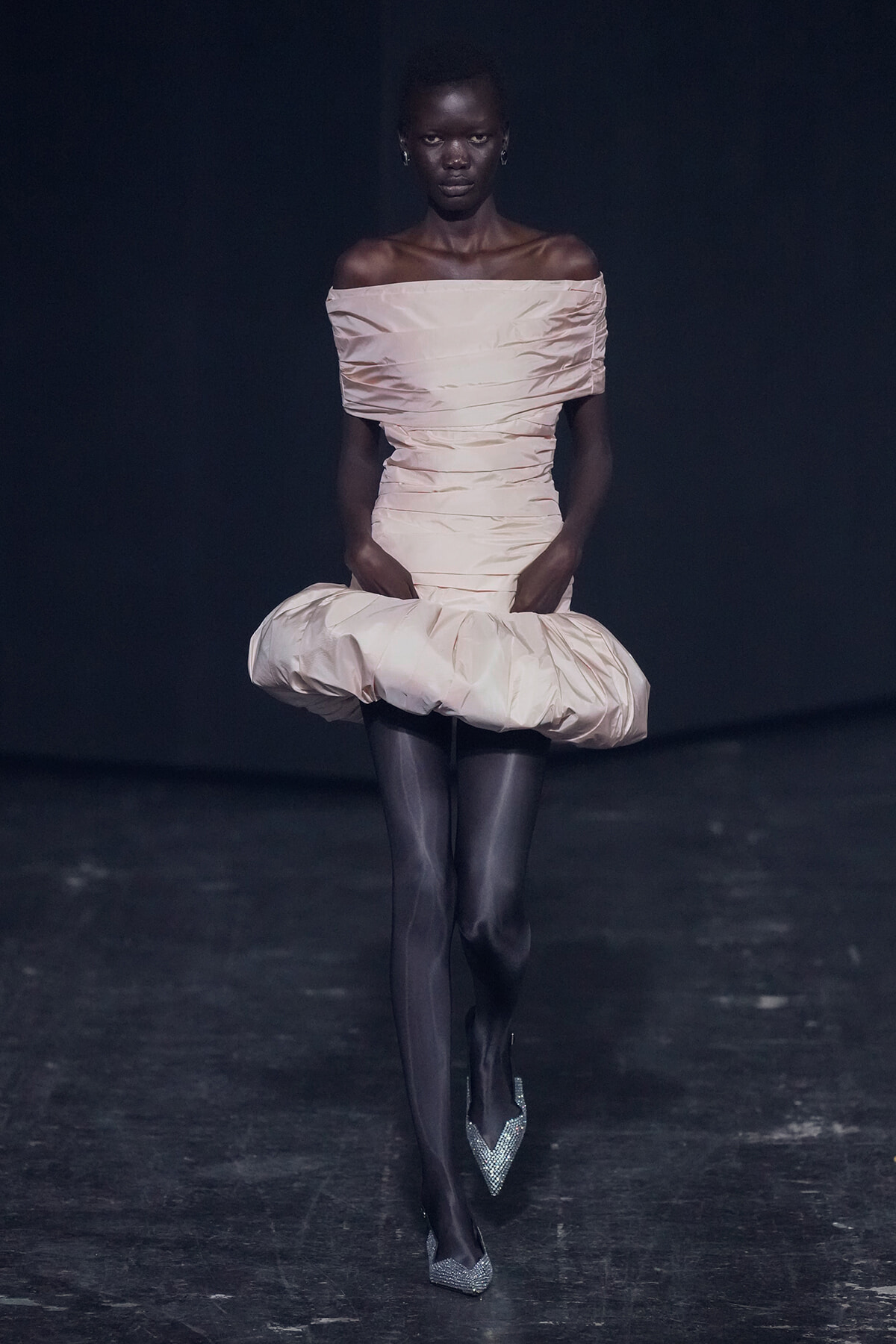 Runway model in a pale pink off-shoulder dress with a large puffed skirt walking the catwalk.