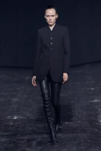 Model walks a runway in a black tailored blazer with large buttons and thigh-high leather boots.